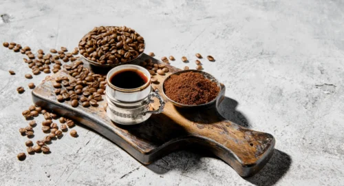 nell'immagine è raffigurato un tagliere con dei chicchi di caffè, del caffè in polvere, e una tazzina di caffè espresso