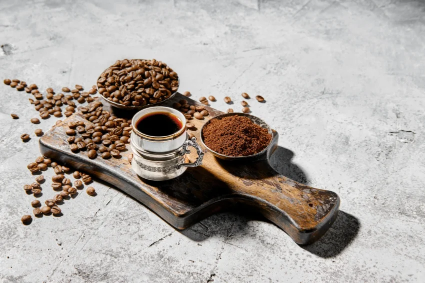 nell'immagine è raffigurato un tagliere con dei chicchi di caffè, del caffè in polvere, e una tazzina di caffè espresso