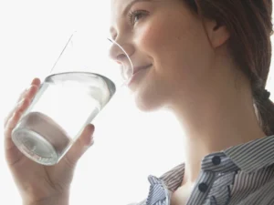 l'immagine di una ragazza che beve un bicchiere di acqua, l'importanza di idratarsi a sufficienza se si soffre di diverticolite