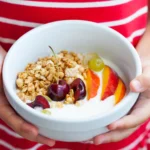 bambina che tiene una ciotola di yogurt con frutta e cereali,uno degli spuntini intelligenti per l'alimentazione di infanzia